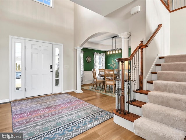 entrance foyer with ornate columns, stairway, arched walkways, and wood finished floors