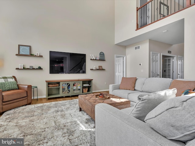 living room with visible vents, a towering ceiling, baseboards, and wood finished floors