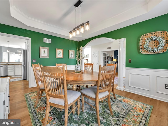 dining room with arched walkways, visible vents, light wood-type flooring, a raised ceiling, and ornate columns