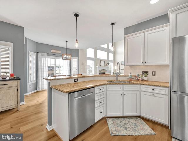 kitchen featuring stainless steel appliances, a peninsula, a sink, and white cabinetry