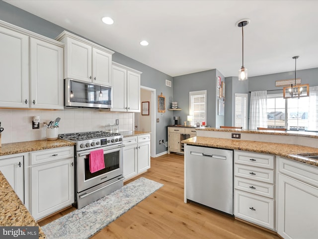 kitchen featuring pendant lighting, stainless steel appliances, tasteful backsplash, light wood-style floors, and white cabinets