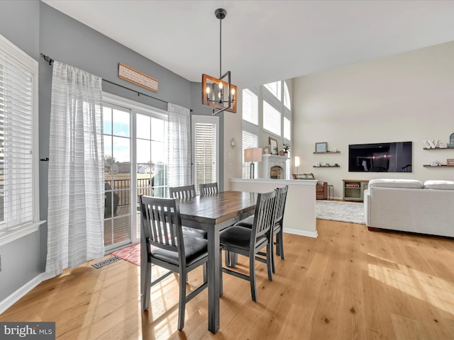 dining space featuring a notable chandelier, a fireplace, visible vents, baseboards, and light wood finished floors