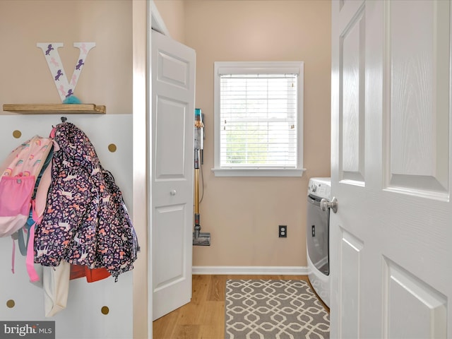 clothes washing area with laundry area, light wood-type flooring, washing machine and clothes dryer, and baseboards