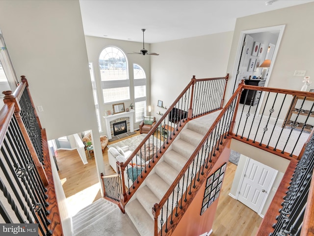 stairway with a towering ceiling, a ceiling fan, a glass covered fireplace, wood finished floors, and baseboards