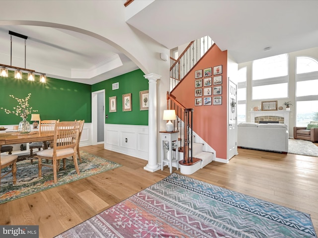 dining room featuring decorative columns, a decorative wall, light wood-style floors, wainscoting, and stairs