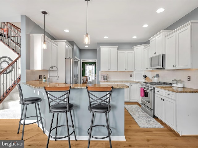 kitchen featuring white cabinets, appliances with stainless steel finishes, a breakfast bar, a peninsula, and pendant lighting