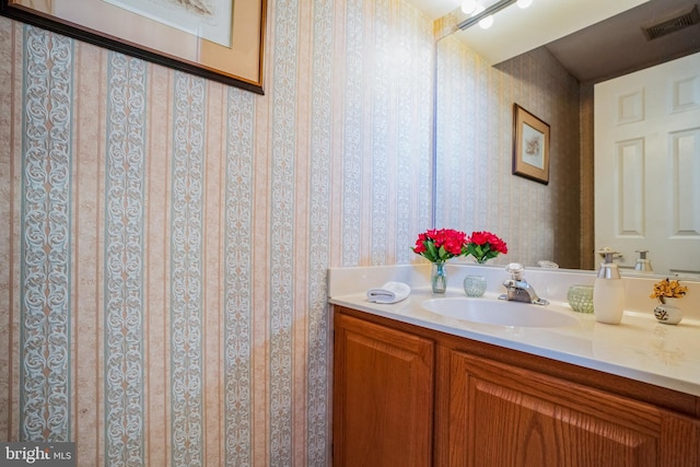 bathroom with visible vents, vanity, and wallpapered walls