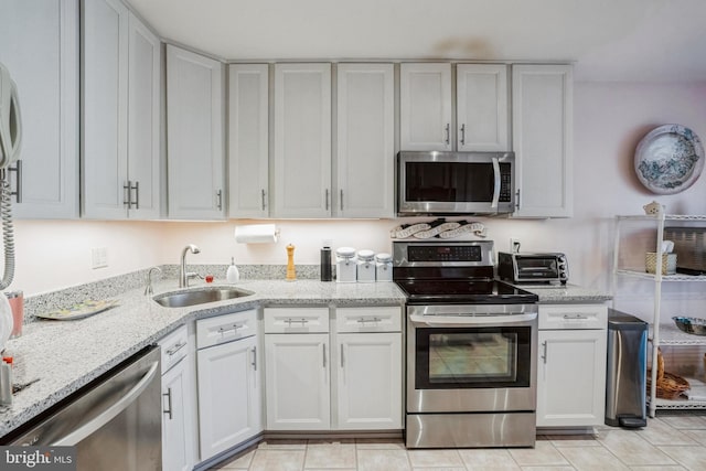 kitchen featuring a toaster, appliances with stainless steel finishes, white cabinetry, a sink, and light stone countertops