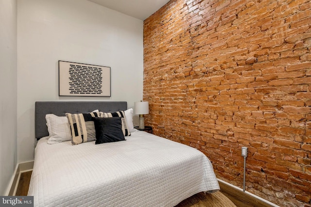 bedroom featuring brick wall, baseboards, and wood finished floors