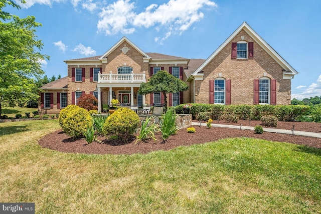 view of front of home with a balcony, a front yard, and brick siding