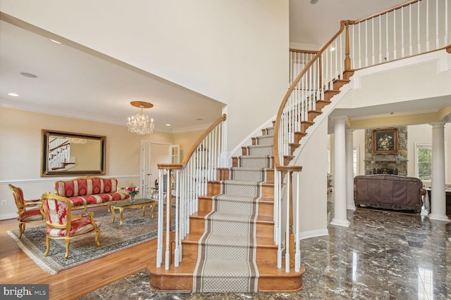 staircase featuring a high ceiling, a fireplace, marble finish floor, decorative columns, and crown molding