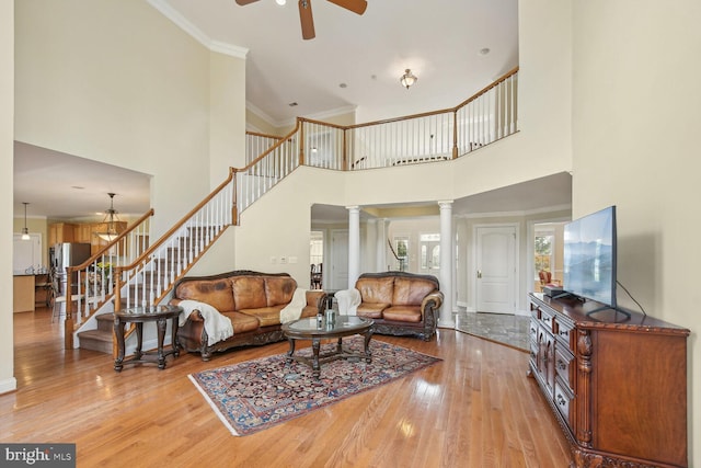 living area featuring ornate columns, crown molding, stairs, and light wood-style floors