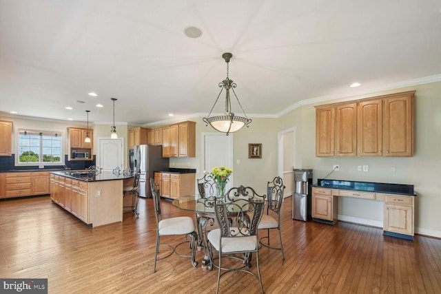 kitchen featuring stainless steel appliances, wood finished floors, a kitchen island, hanging light fixtures, and dark countertops