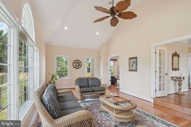 living area featuring a ceiling fan, baseboards, high vaulted ceiling, and wood finished floors