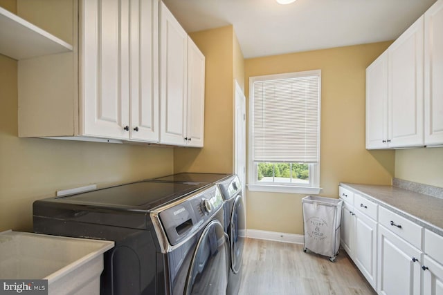 washroom featuring light wood-style flooring, a sink, baseboards, cabinet space, and washing machine and clothes dryer