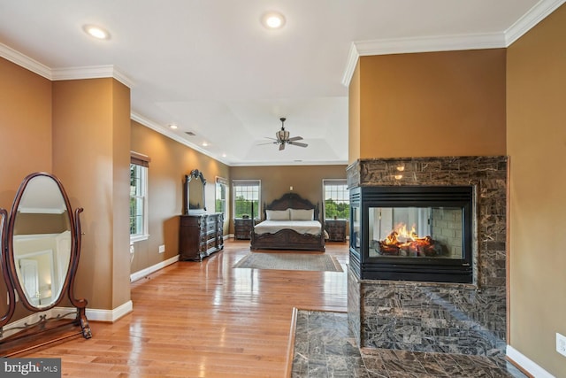 bedroom featuring light wood finished floors, baseboards, crown molding, and a multi sided fireplace