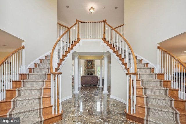 entrance foyer with marble finish floor, decorative columns, stairway, and a high ceiling