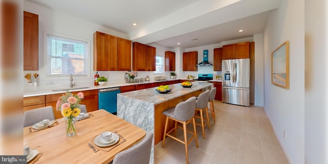 kitchen with a center island, light countertops, appliances with stainless steel finishes, a sink, and wall chimney exhaust hood