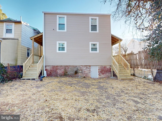 rear view of house featuring entry steps, fence, and stairs