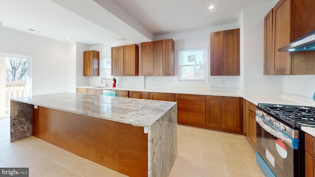 kitchen featuring light tile patterned floors, brown cabinetry, wall chimney exhaust hood, a center island, and stainless steel range with gas cooktop