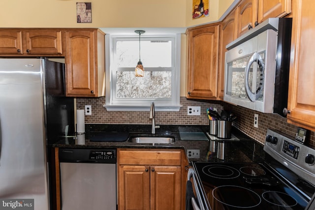 kitchen with stainless steel appliances, a sink, brown cabinets, tasteful backsplash, and dark stone countertops