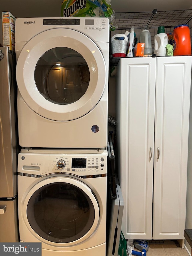 clothes washing area with light tile patterned floors, cabinet space, and stacked washer / drying machine