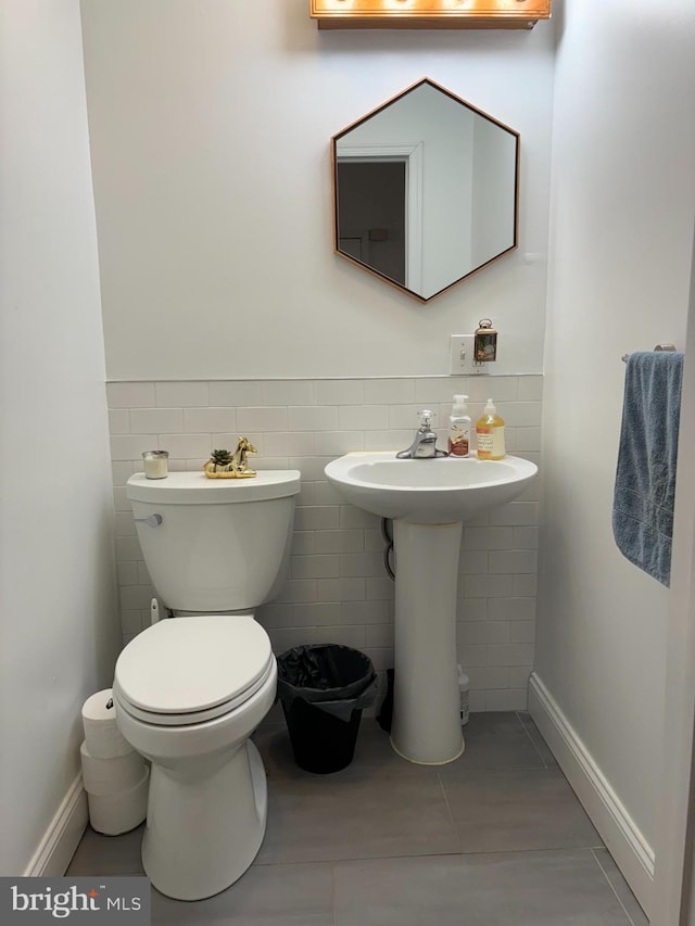 half bath featuring toilet, tile patterned flooring, tile walls, and wainscoting