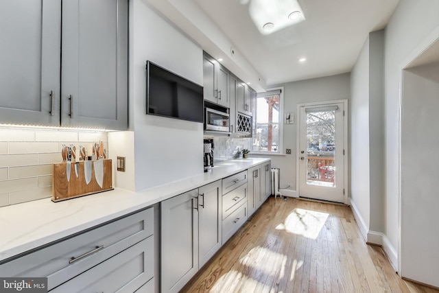 kitchen with tasteful backsplash, stainless steel microwave, light wood-style flooring, gray cabinetry, and baseboards