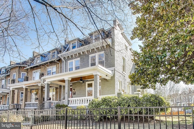 view of front of home featuring a fenced front yard, mansard roof, a ceiling fan, and brick siding