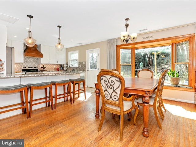 dining room featuring light wood finished floors, visible vents, and an inviting chandelier