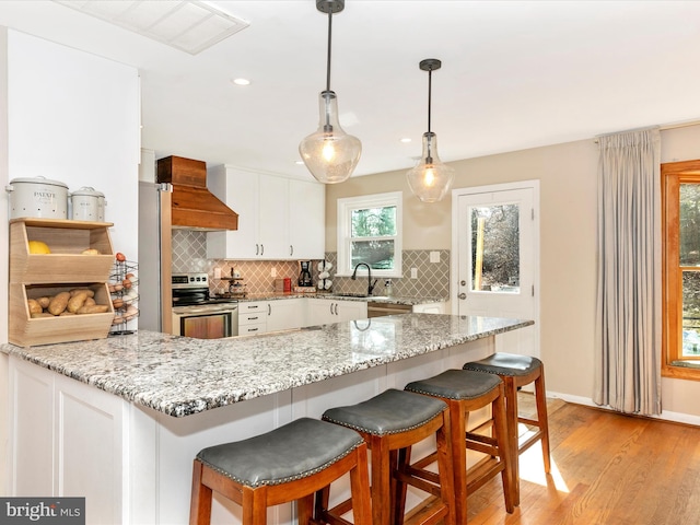 kitchen with electric stove, custom range hood, white cabinetry, a sink, and a peninsula