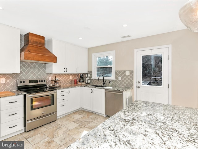 kitchen with stainless steel appliances, tasteful backsplash, custom range hood, white cabinetry, and a sink