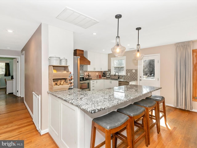 kitchen featuring a peninsula, premium range hood, stainless steel appliances, a sink, and white cabinets