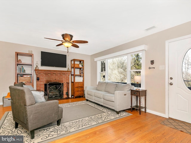 living room with ceiling fan, a fireplace, visible vents, baseboards, and light wood-style floors