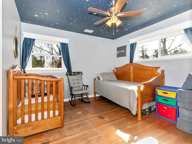 bedroom featuring multiple windows, visible vents, baseboards, and wood finished floors