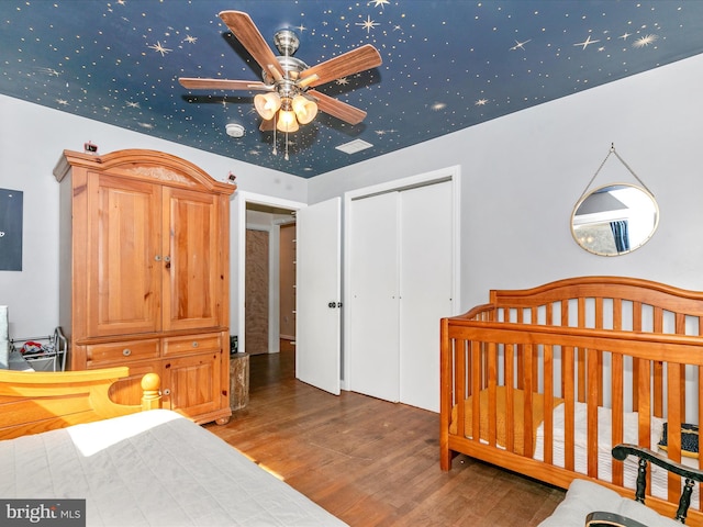 bedroom featuring a crib, a closet, visible vents, and wood finished floors