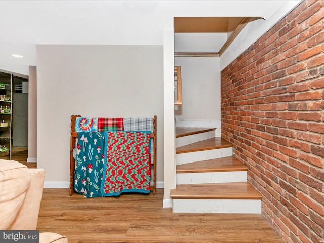 stairway featuring baseboards, brick wall, and wood finished floors