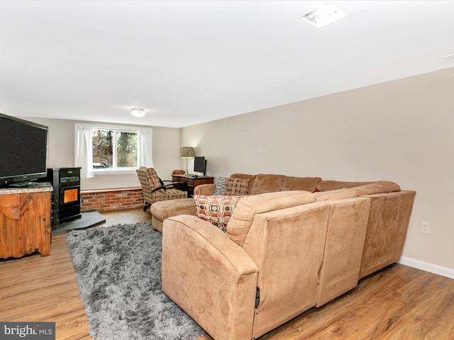 living room featuring a wood stove, brick wall, light wood-style flooring, and baseboards