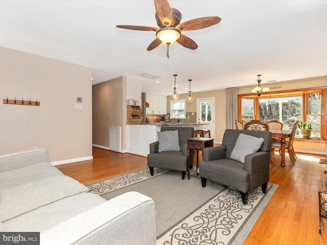 living room featuring light wood-type flooring, visible vents, baseboards, and ceiling fan with notable chandelier