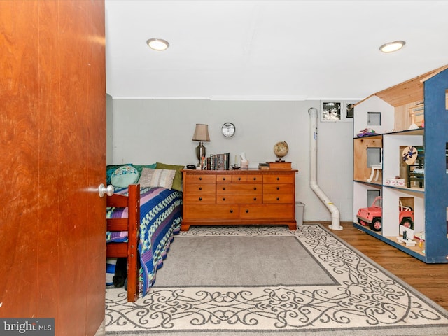 bedroom with wood finished floors, concrete block wall, and recessed lighting