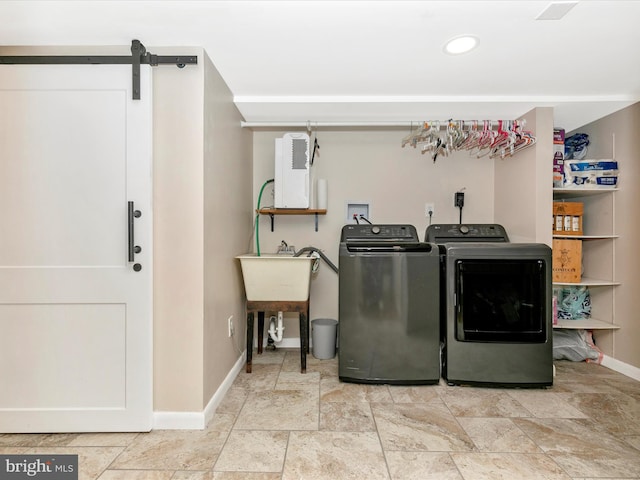 clothes washing area featuring a barn door, baseboards, stone finish floor, washer and dryer, and recessed lighting