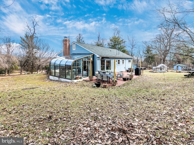 rear view of house featuring a sunroom, a patio area, a yard, and a chimney