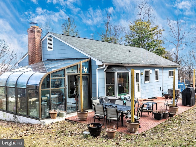 rear view of property featuring a shingled roof, a patio, a sunroom, a chimney, and cooling unit