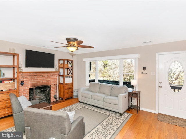 living area with a fireplace, light wood finished floors, visible vents, ceiling fan, and baseboards