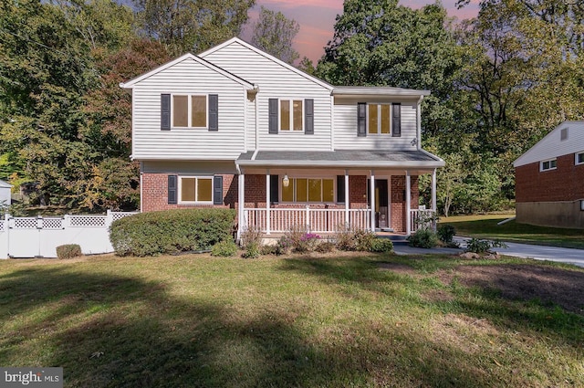 view of front of property with covered porch, brick siding, fence, and a lawn