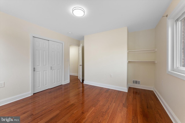 unfurnished bedroom featuring visible vents, a closet, baseboards, and wood finished floors