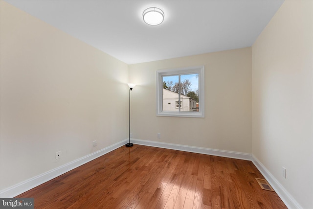 empty room with wood-type flooring, visible vents, and baseboards