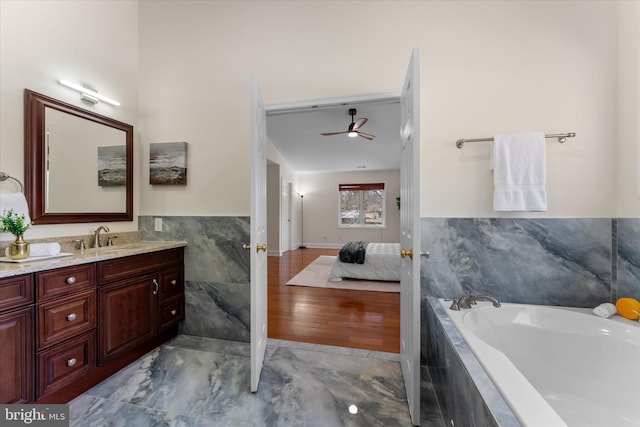 ensuite bathroom with a garden tub, connected bathroom, a ceiling fan, vanity, and tile walls