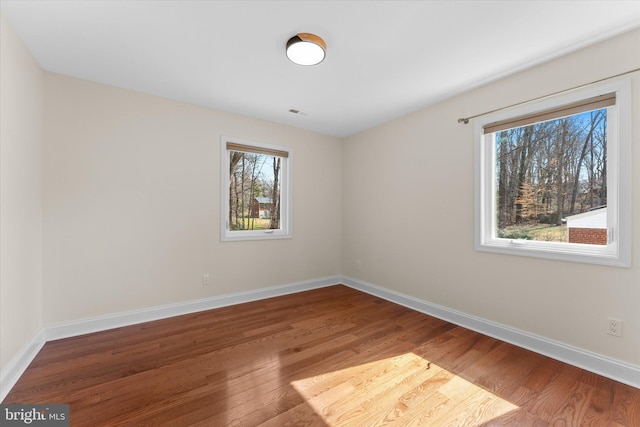 spare room featuring wood finished floors, visible vents, and baseboards