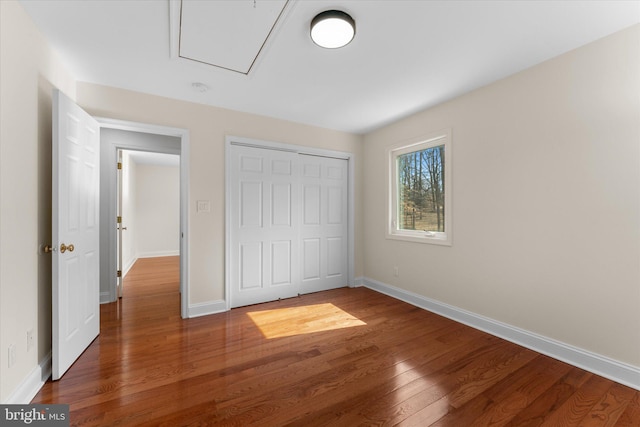 unfurnished bedroom with attic access, a closet, baseboards, and wood finished floors